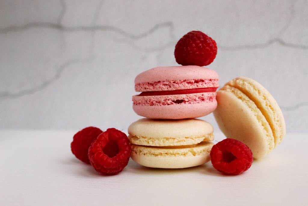 White and pink macaroon cakes with raspberries on an abstract gray background. 